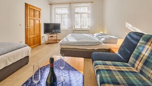 Una habitación con una cama, un sofá, un televisor, un armario de madera y una ventana con cortinas.