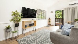 En moderne stue med et fladskærms-tv, potteplanter, en grå sofa og en tæppe med mønster.