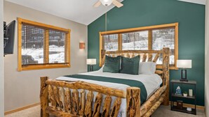 Une chambre à coucher avec un lit en bois, deux tables de chevet et une fenêtre avec des stores.