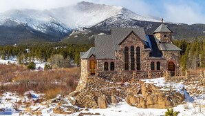 Une église en pierre dotée d’un clocher, se dressant sur un fond de montagnes enneigées et d’un ciel dégagé.