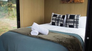 Un lit bien fait, avec une couvre-lit bleue et une couverture marron, deux coussins à carreaux et une serviette blanche enroulée posée sur le lit.