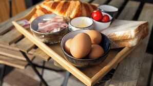 Une table en bois sur laquelle se trouve un plateau avec une baguette, des œufs, un bol de tomates et un bol de viande.