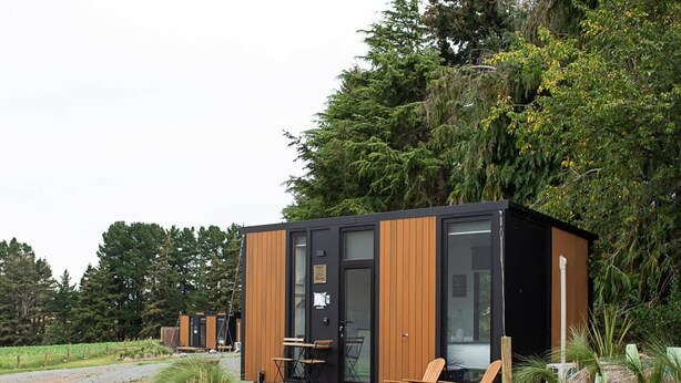 Une cabane moderne avec une façade en bois, de grandes fenêtres et un sol en gravier.