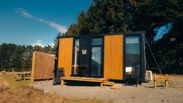 Uma cabana com fachada de madeira, janelas amplas e um banco na parte externa.