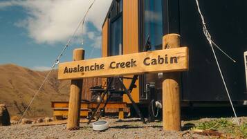 A wooden sign for 'Avalanche Creek Cabin' with a rustic outdoor setting, including a wooden bench and a dog bowl.
