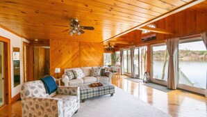 A cozy cabin interior with a wooden ceiling, a sofa, a matching armchair, and a dining area.