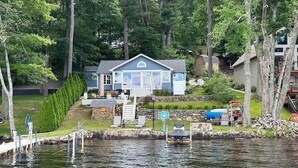 A lakeside house with a dock, a covered deck, and a stone wall.