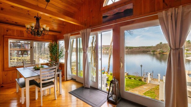 A wooden cabin with a dining area, large windows, and a view of a lake.