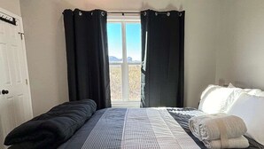 A room with a bed, a window with curtains, a door, and a view of the outdoors. - Desert Quail Oasis: Style, Comfort & Easy Access (Terlingua)