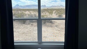 A window with a view of a desert landscape, including mountains and sparse vegetation. - Desert Quail Oasis: Style, Comfort & Easy Access (Terlingua)