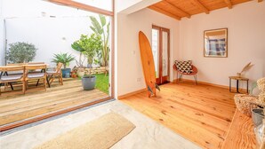 Una habitación amplia con suelo de madera, un ventanal grande y una tabla de surf apoyada en la pared.