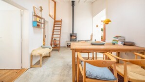 Una habitación acogedora con una mesa de madera, sillas, un banco, una escalera, una estantería, una chimenea y una lámpara colgante.
