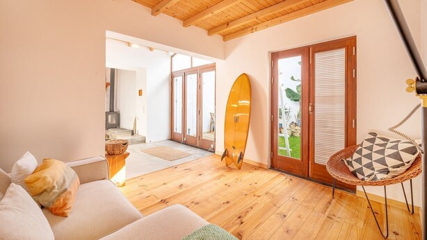 Una sala de estar acogedora con techo de madera, un sofá, una tabla de surf y un sillón de mimbre.