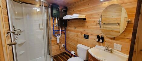 Un bagno con rivestimenti in legno, cabina doccia in vetro, un water, un lavandino e uno specchio.