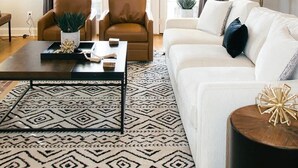 Un salon comprenant un canapé, deux fauteuils, une table basse et un tapis à motifs.