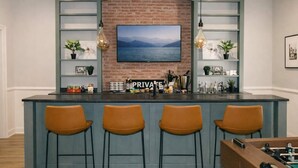 Un espace bar avec un mur en briques, un téléviseur fixé au mur et des tabourets de bar.