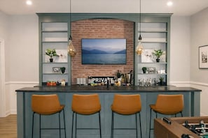 A bar area with a brick wall, a mounted TV, and bar stools. - Charming Sylvan Park Home • Relax & Stay (Nashville)