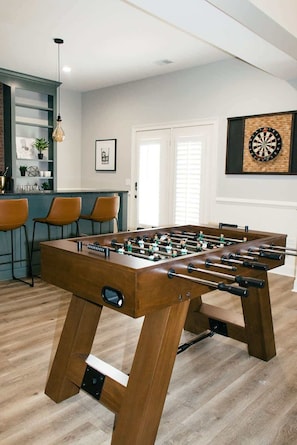 A foosball table in a room with a bar area, a dartboard, and a framed picture on the wall. - Charming Sylvan Park Home • Relax & Stay (Nashville)