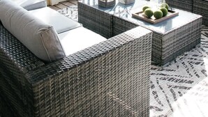 Un espace extérieur ensoleillé, aménagé avec des meubles en osier, une table basse en verre et un plateau de fruits.
