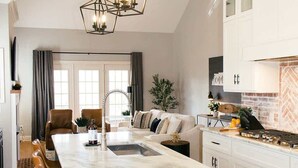 Une cuisine moderne dotée d’un îlot en marbre, de meubles blancs et d’un luminaire suspendu au design géométrique original.