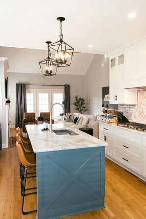 A modern kitchen with a marble island, white cabinetry, and a unique geometric pendant light.