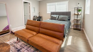 A modern bedroom with a brown leather sofa, a bed with grey bedding, a standing desk, and a plant on a metal shelf. - Cozy Downtown, Montrose Studio!
Free parking ! (Houston)