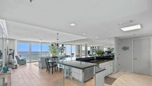 A modern kitchen with a large island, a dining area with a view, and a spacious living area with a large window overlooking the ocean.