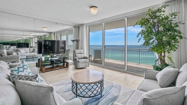 A spacious living room with a large window overlooking the ocean, a comfortable seating area, and a television.