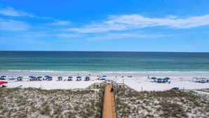 A beach with a wooden boardwalk leading to the shore, umbrellas, and beach chairs.