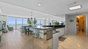 A modern kitchen with a large island, a dining area with a view, and a spacious living area with a balcony overlooking the sea.
