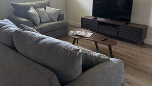 A modern living room with a grey sofa, a coffee table, a flat-screen TV, and a ceiling fan. - Close to hiking trails, Central home, 3 bedrooms! (Phoenix)