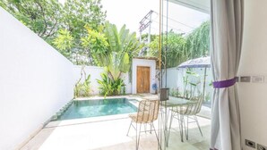 Un espace piscine privatif agrémenté d’une paroi en verre, de deux fauteuils en osier et d’une petite table.