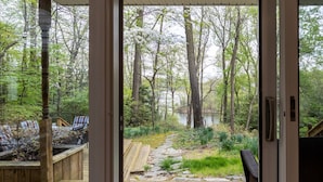 Eine Holzterrasse führt zu einem bewaldeten Gebiet mit Teich, Sitzgelegenheiten im Freien und einem Grill.