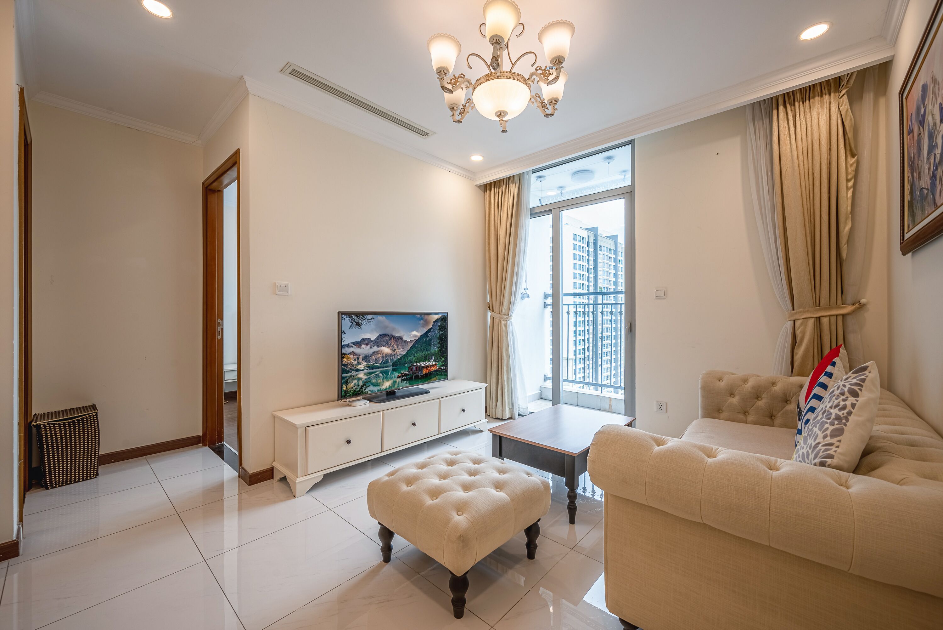 A modern living room with a television, sofa, ottoman, and a large window with curtains.