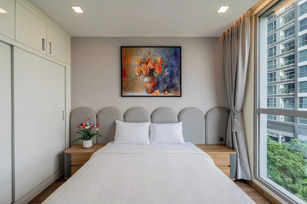 Une chambre à coucher moderne, avec un grand lit, un tableau accroché au mur et une vue sur la ville par la fenêtre.