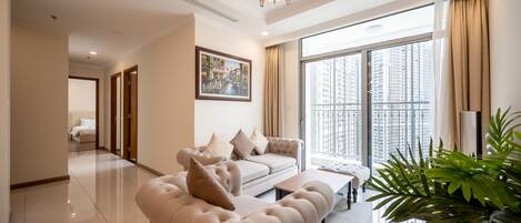 A spacious living room with a beige sofa, a coffee table, and a large window offering a city view.