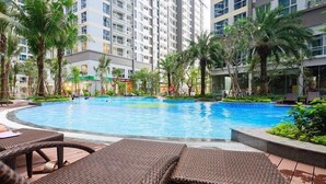 A swimming pool surrounded by lounge chairs and palm trees, with a high-rise building in the background. - Vinhomes Central Park - KIMI Residences (Ho Chi Minh City)
