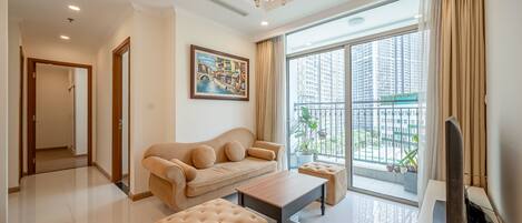 A modern living room with a sofa, ottoman, and coffee table, large windows with a view of high-rise buildings, and a chandelier.