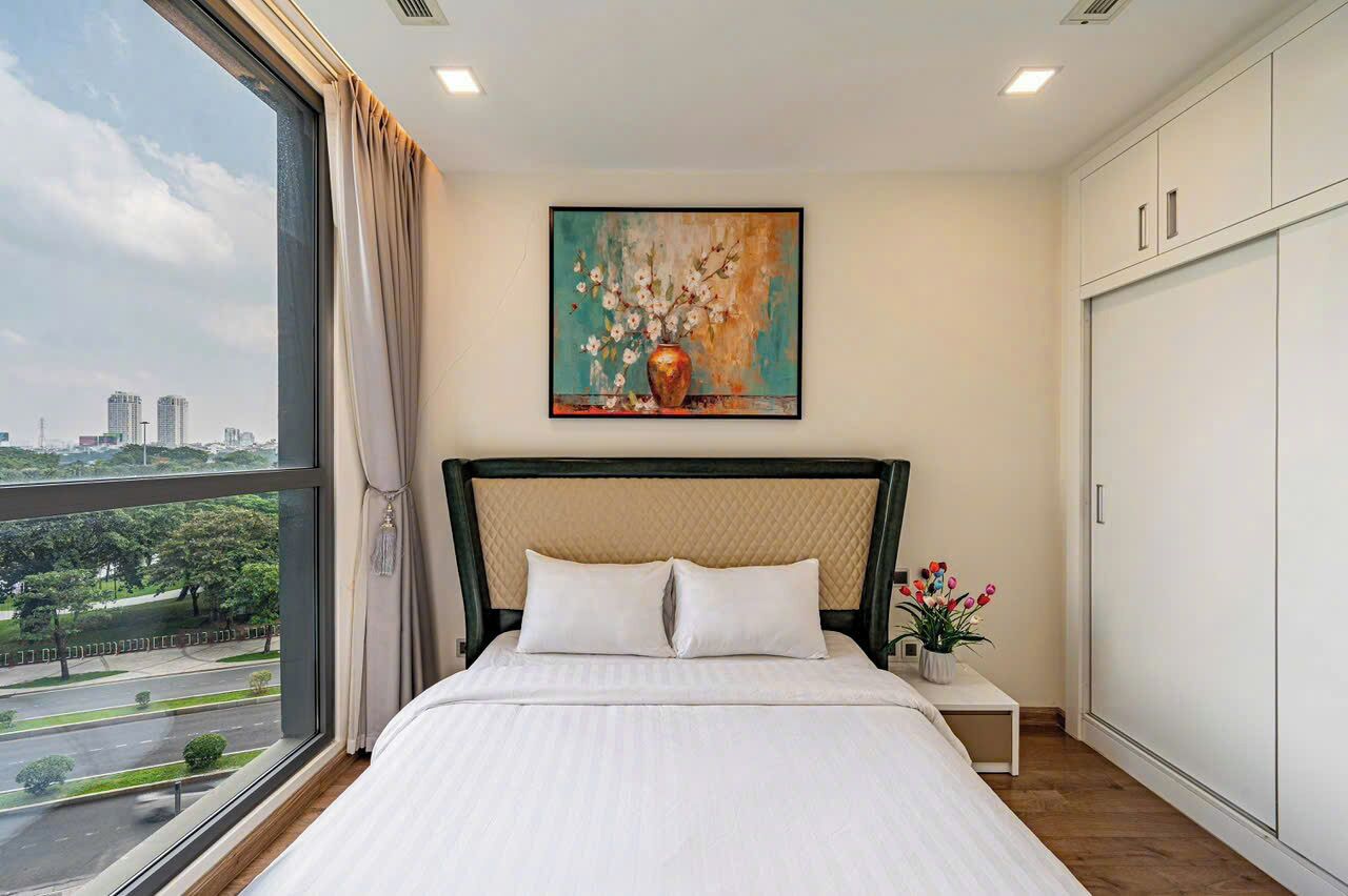 A hotel room with a large window, a bed with white bedding, a painting on the wall, and a wardrobe.