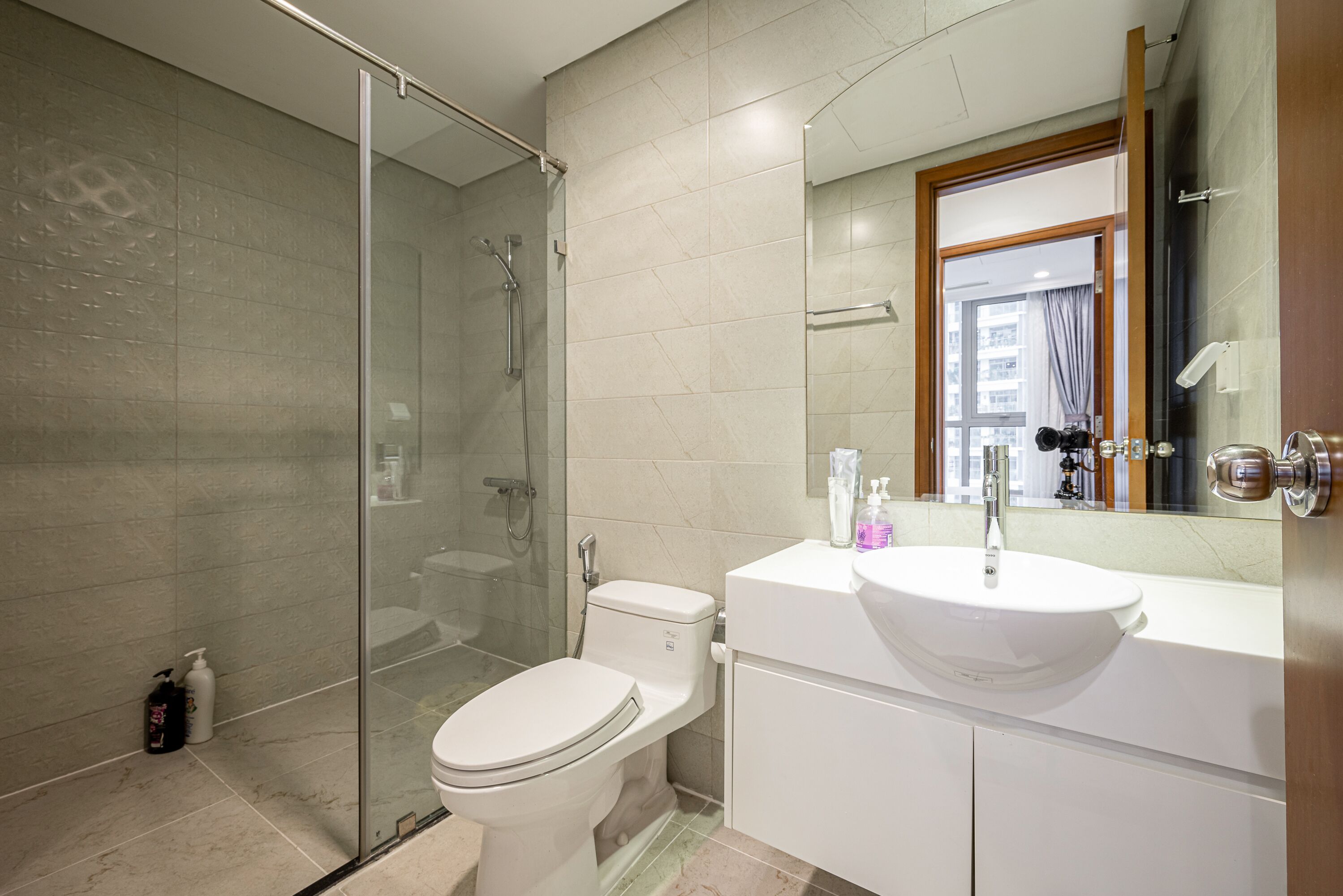 A modern bathroom with a glass-enclosed shower, a white toilet, and a large sink with a mirror above it.