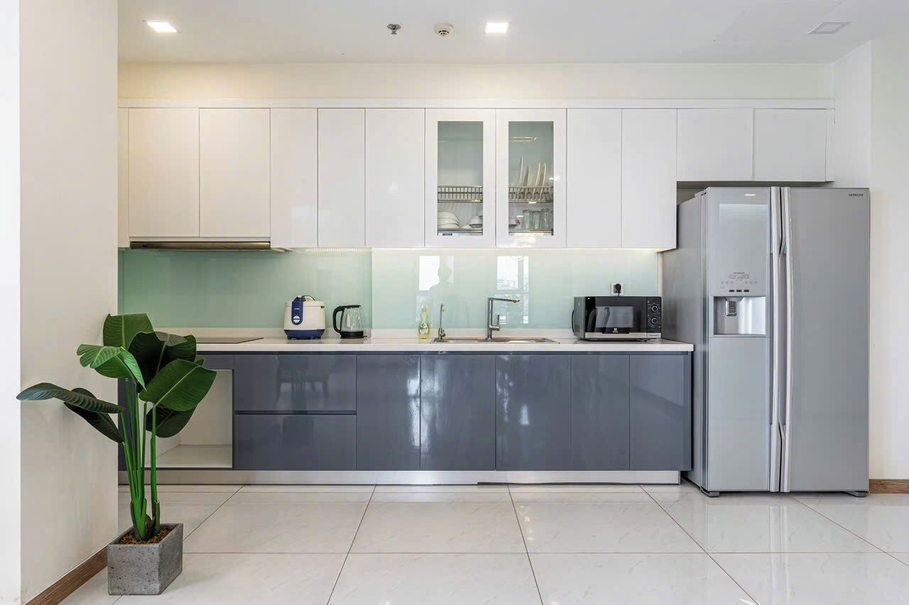 Una cocina moderna con armarios blancos, un refrigerador de acero inoxidable, horno empotrado y cafetera.