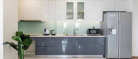 Una cocina moderna con armarios blancos, un refrigerador de acero inoxidable, horno empotrado y cafetera.