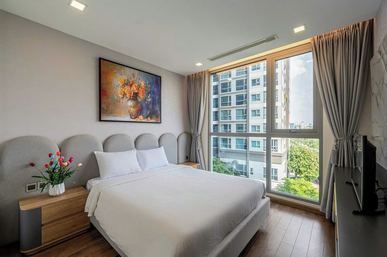 A modern hotel room with a large bed, a painting on the wall, a window with curtains, and a view of a building.