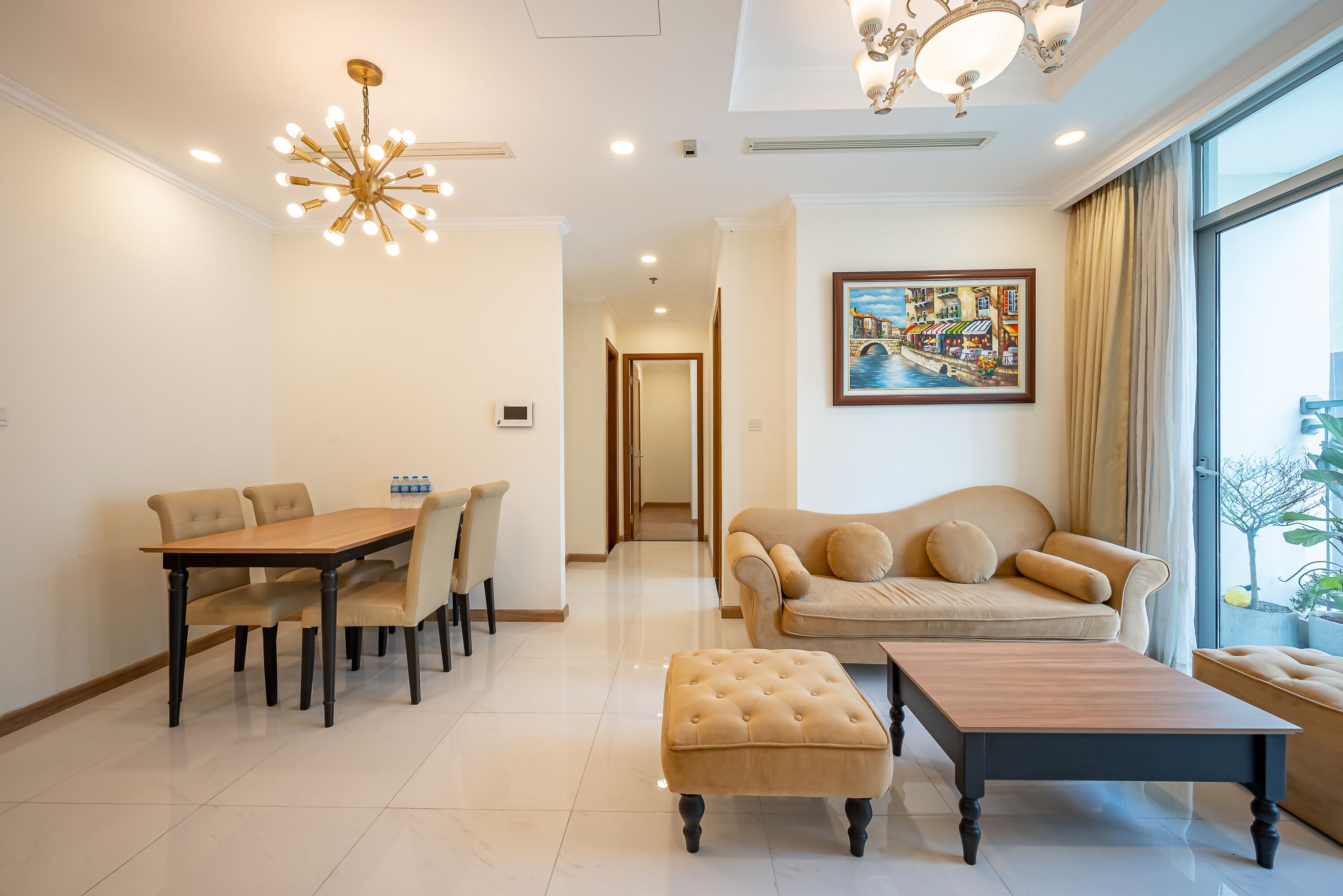 A spacious living room with a dining table, sofa, ottoman, and a large window with a view.