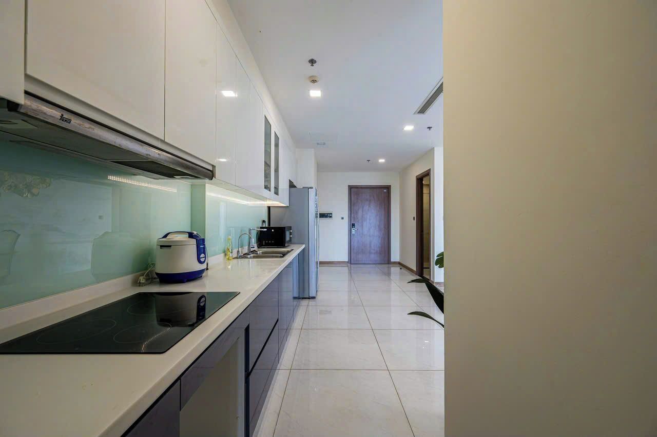 A modern kitchen with a black induction cooktop, a built-in oven, and a microwave. There is a window with a view of the outside, and a door leading to another room.