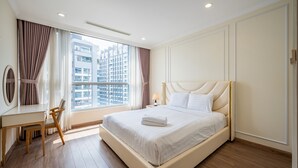 A hotel room with a large bed, a desk, and a chair. - Vinhomes Central Park - KIMI Residences (Ho Chi Minh City)