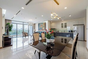 A modern living room with a dining area, large windows, and a kitchen. - Vinhomes Central Park - KIMI Residences (Ho Chi Minh City)