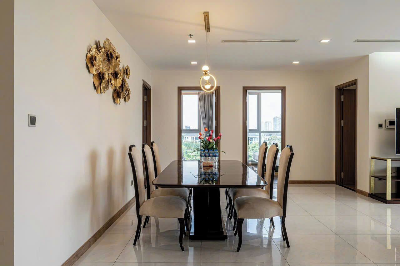 A dining area with a rectangular table, six chairs, a chandelier, and a decorative wall piece.