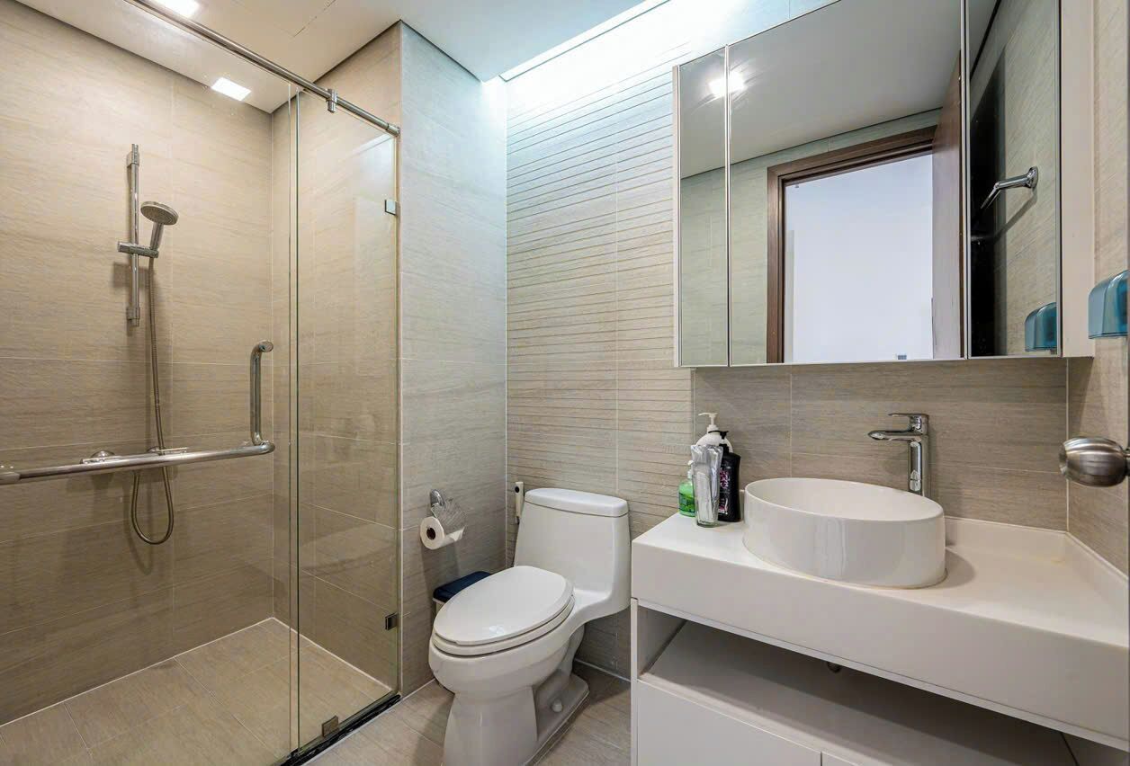 A modern bathroom with a glass shower enclosure, a toilet, and a vanity with a sink and mirror.