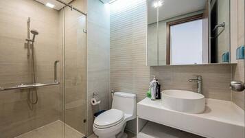 A modern bathroom with a glass shower enclosure, a toilet, and a vanity with a sink and mirror.